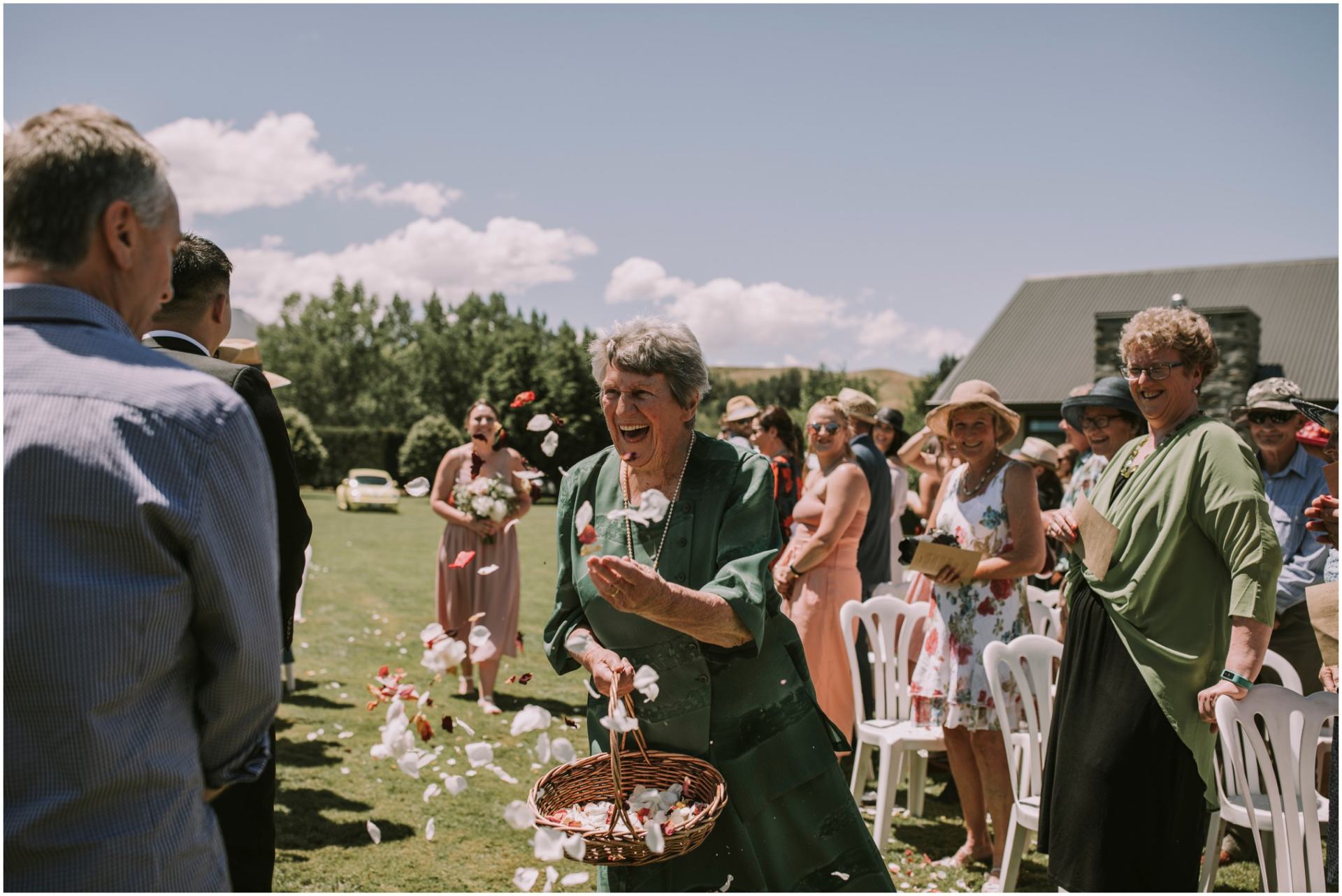 Charlotte Kiri Photography - Wedding Photography of a Mother of the bridal party wearing a forest green dress, scattering red and white rose petals as the bride and groom walk down the aisle in Queenstown, New Zealand.