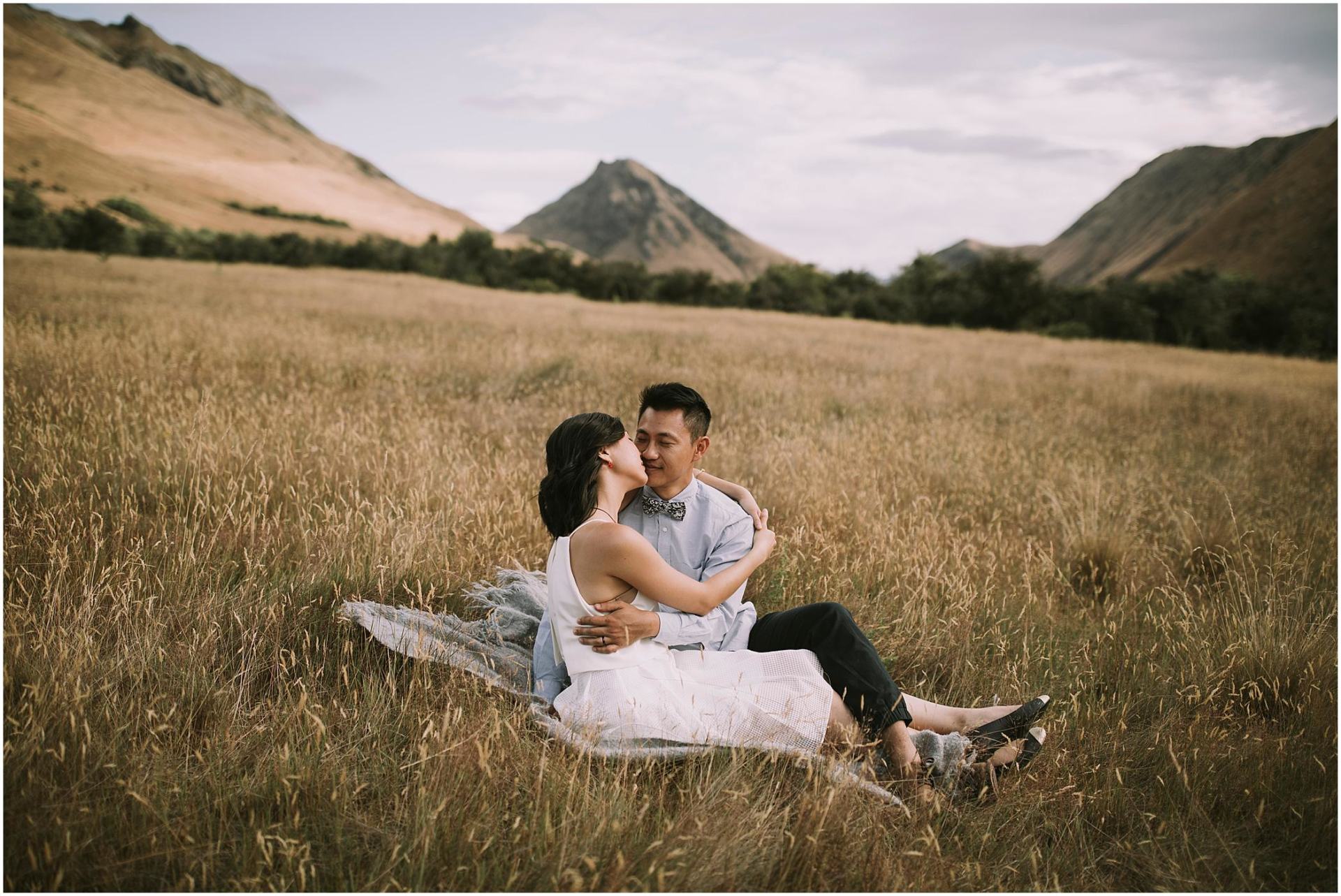 Charlotte Kiri Photography - Engagement Photography with a besotted couple joyfully embracing in the grass with a beautiful mountain landscape behind in Wanaka, New Zealand