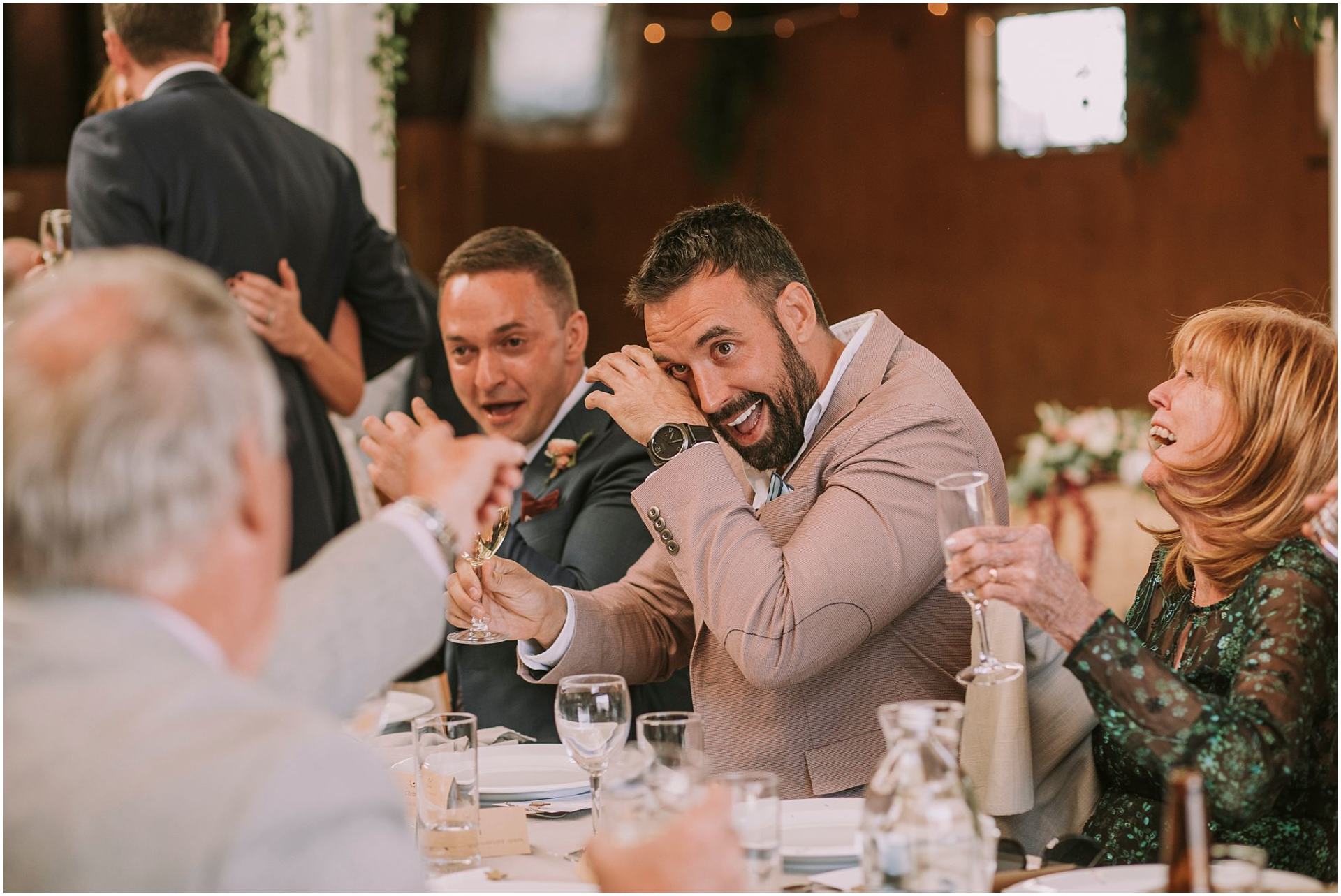 Charlotte Kiri Photography - Wedding Photography of a wedding reception, with guests crying with laughter as they chat over champagne, at a long table, in Queenstown, New Zealand.