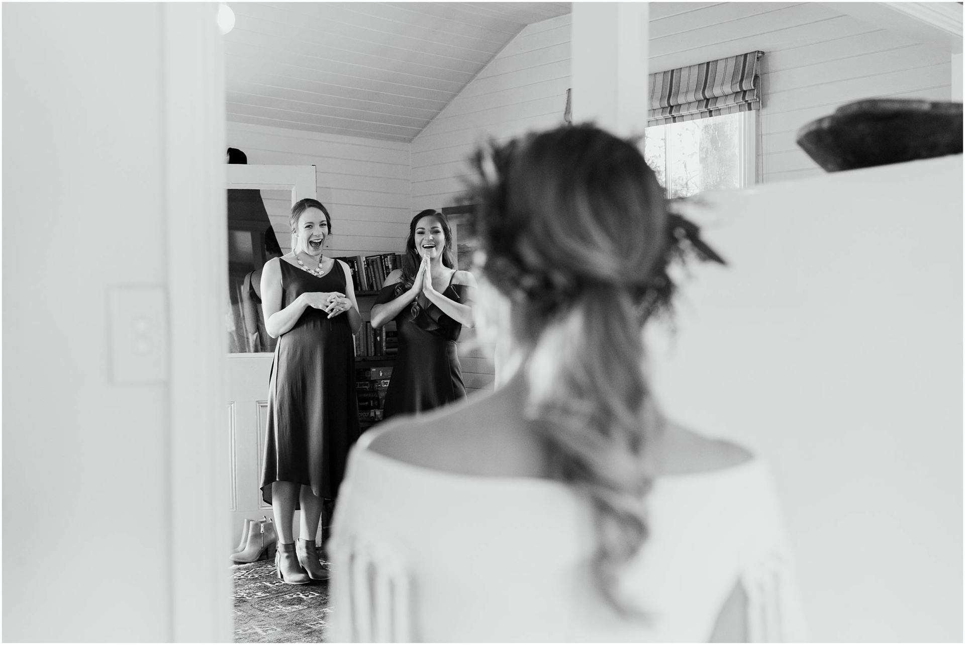 Charlotte Kiri Photography - Wedding Photography of a black and white image of a bride revealing her gown and hair to her bridemaids, as they beam with joy and excitement, in Wanaka, New Zealand.