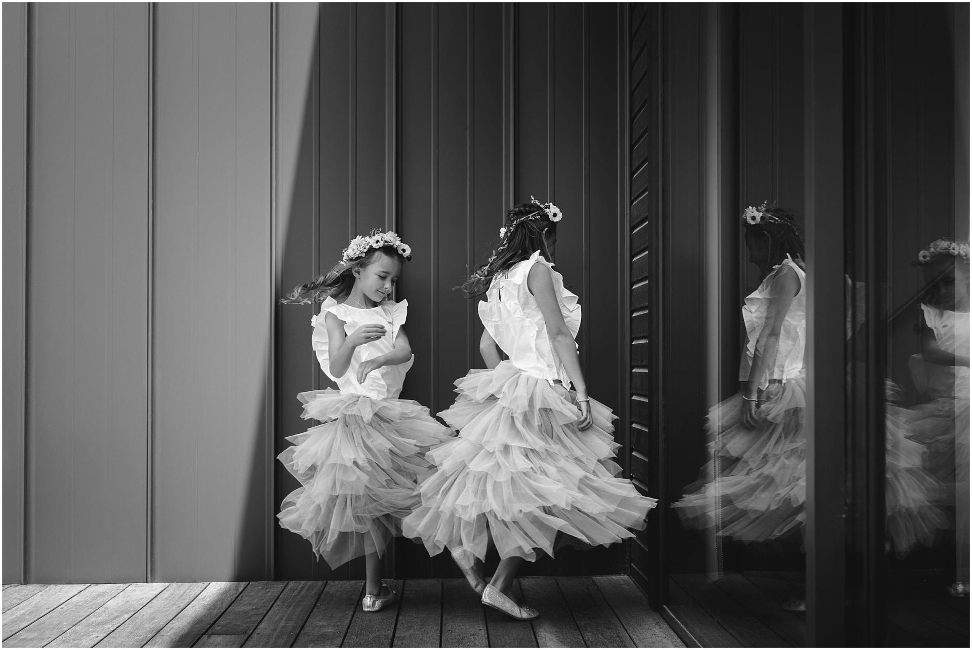 Charlotte Kiri Photography - Wedding Photography of a couple of bridesmaids wearing floral wreaths and spinning their pretty tiered skirts in the mirror in black and white, in Wanaka, New Zealand.