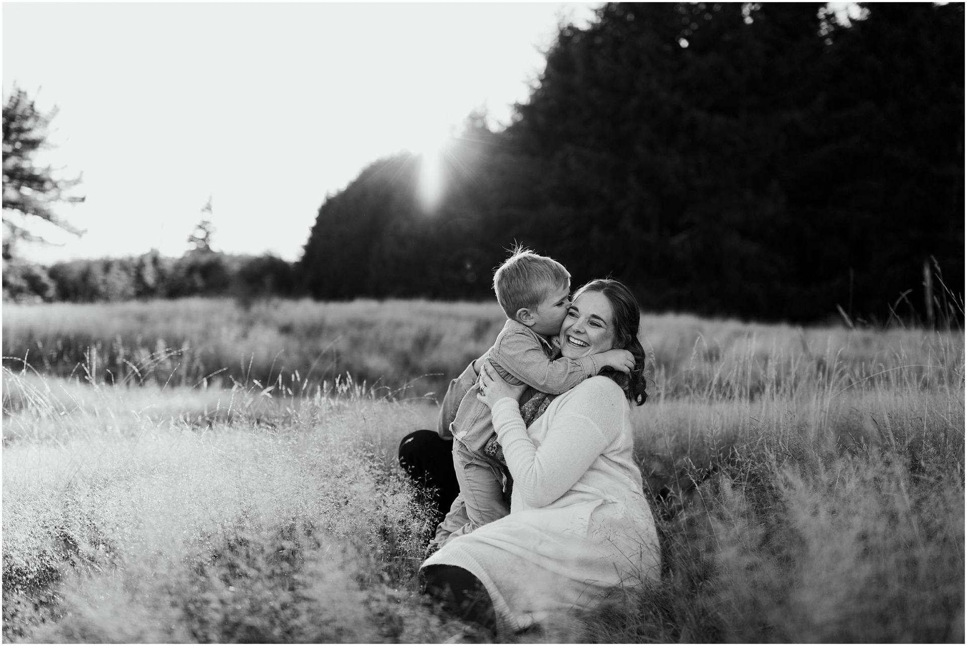 Charlotte Kiri Photography - Family Photography of a mother cuddling her son as he kisses her cheek in a field as the sun goes down behind a line of trees in Wanaka, New Zealand.
