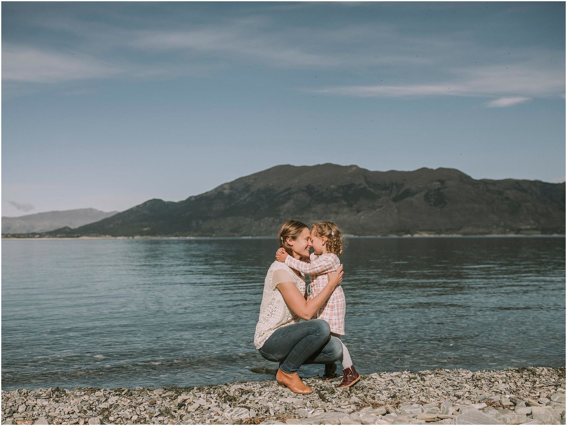 Charlotte Kiri Photography - Family Photography of a mother and daughter cuddling and pressing foreheads, together fondly, in front of a lake with mountains behind in Wanaka, New Zealand.