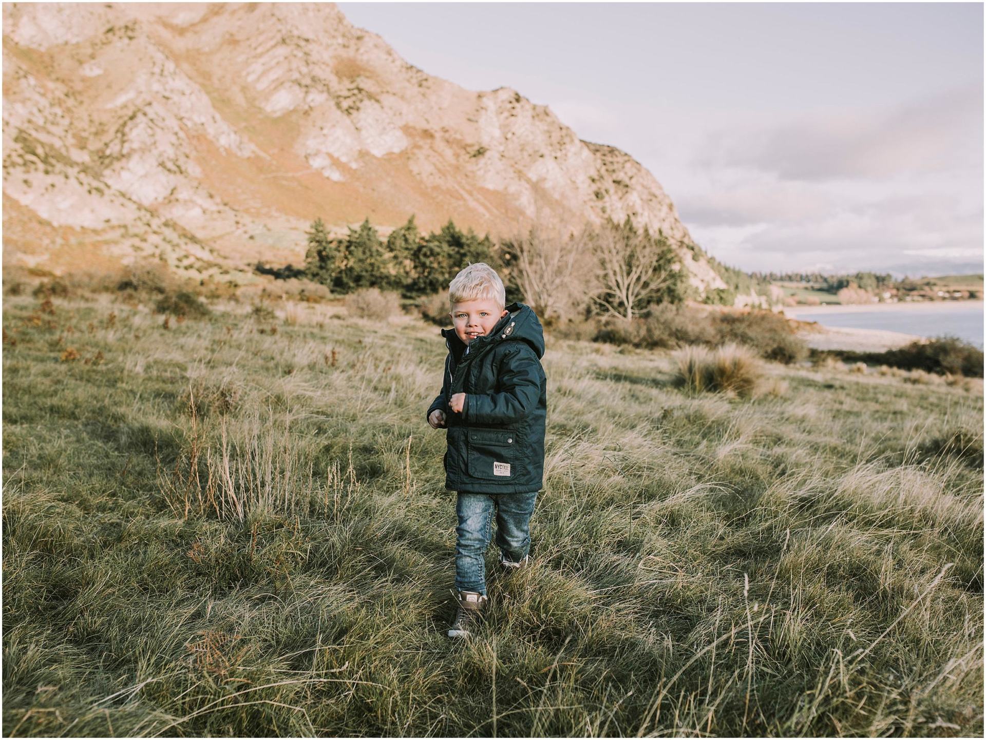 Charlotte Kiri Photography - Family Photography of a toddler running joyfully in a field on the edge of a lake in front of a mountain in Wanaka, New Zealand.