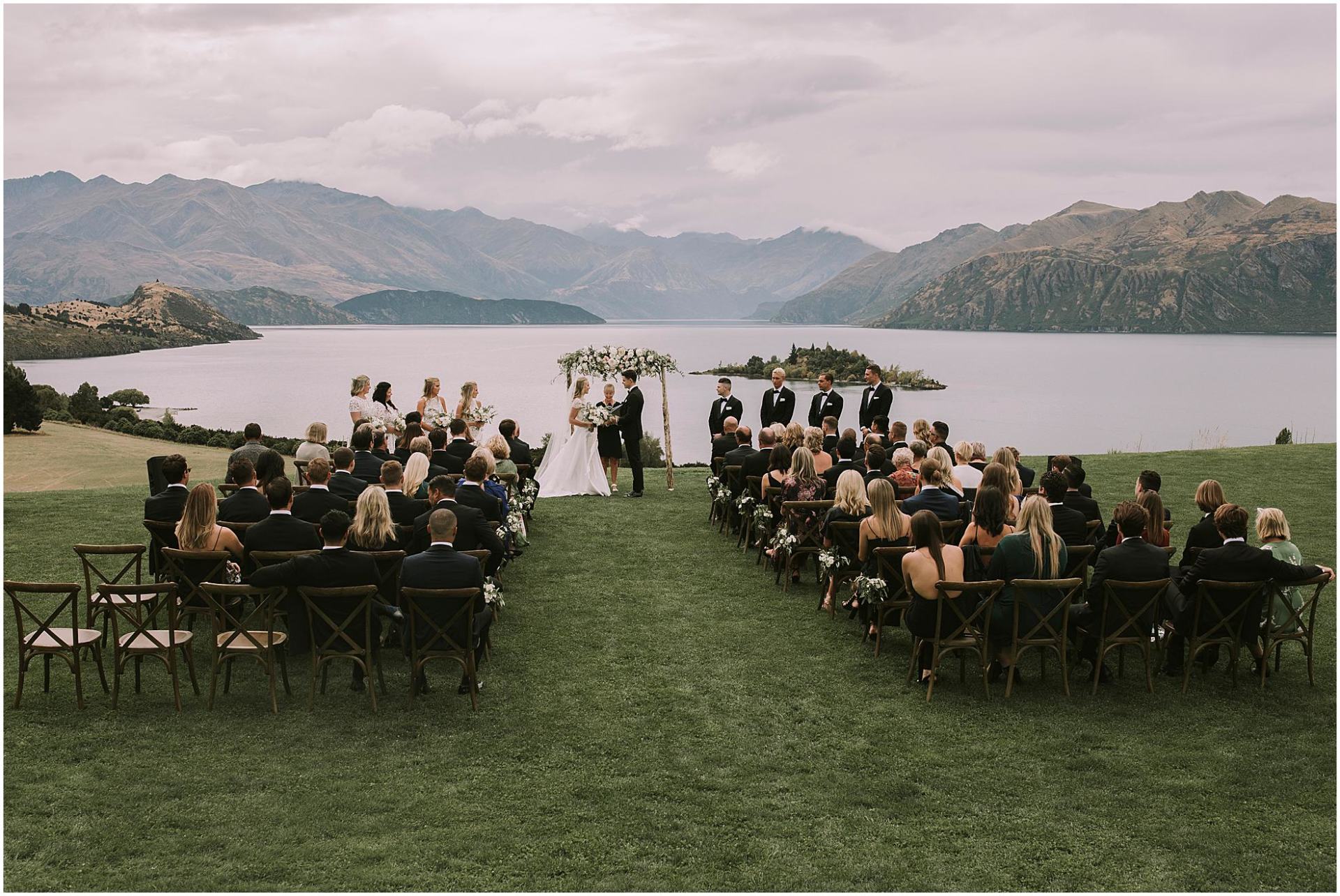 Charlotte Kiri Photography - Wedding Photography of a bride and groom exchanging vows in front of a floral alter with a spectacular backdrop of lakes and mountains behind them at Rippon, in Wanaka, New Zealand.