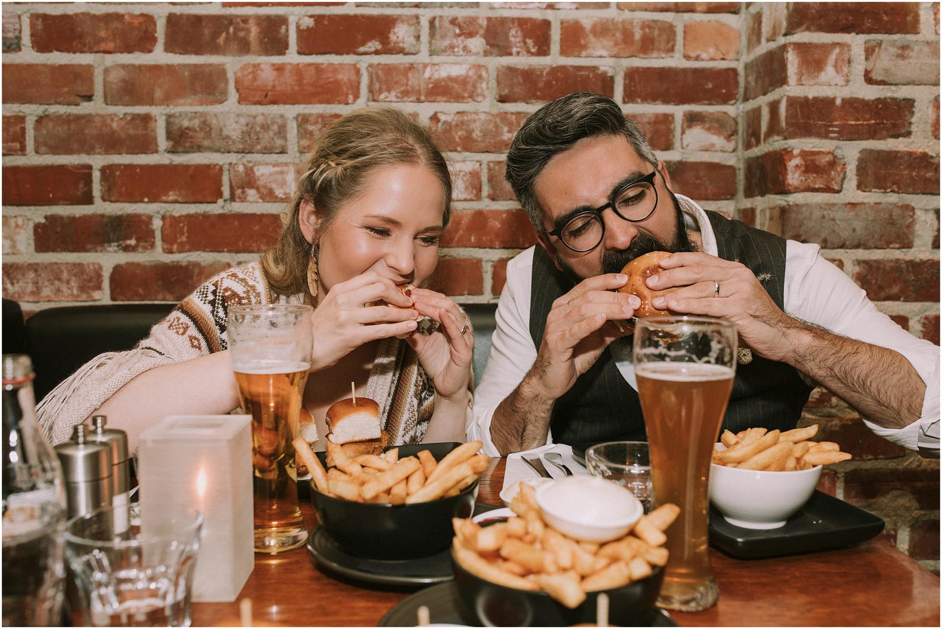 Charlotte Kiri Photography - elopement photography with bride and groom enjoying eating burgers and fries accompanied by a glass of beer at a local restaurant in Wanaka, New Zealand