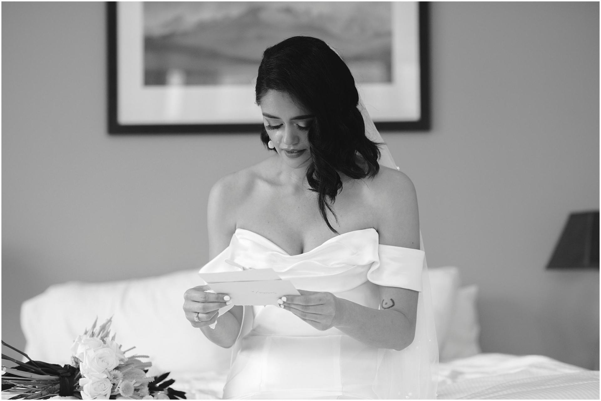 Charlotte Kiri Photography - Elopement Photography of bride wearing sculptured strapless gown with off-shoulder details, reading a letter and crying whilst she sits on the bed of her room, before the ceremony in Wanaka, New Zealand