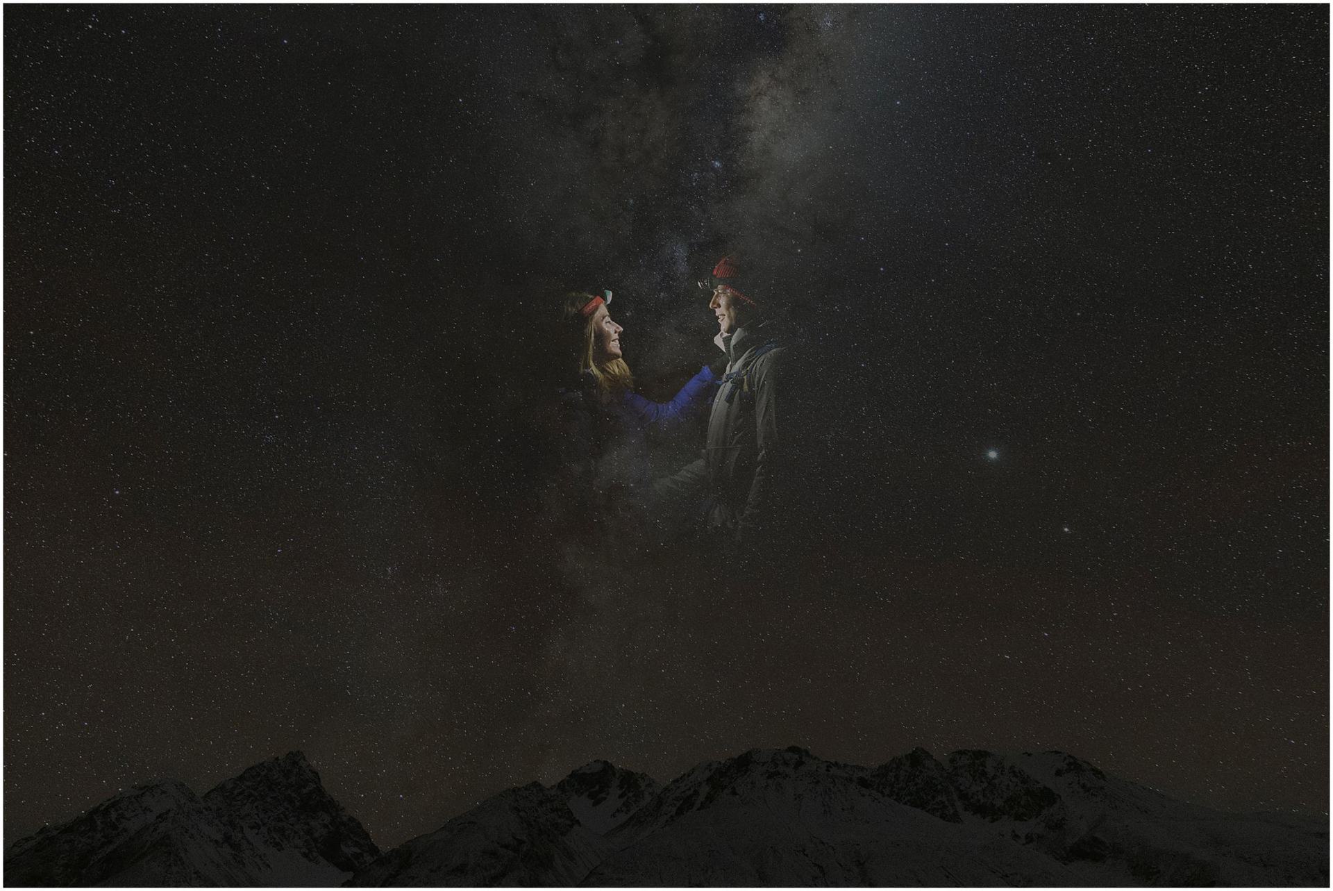 Charlotte Kiri Photography - Engagement Photography of a happy couple wearing explorer outfits seemingly drifting among the celestial milky way in the sky with a silhouette of mountain tops below in Wanaka, New Zealand