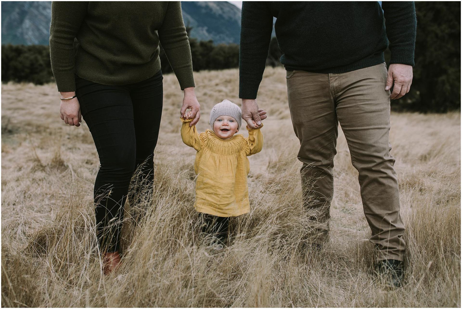 Charlotte Kiri Photography - Family Photography of a couple holding hands with a young child as they walk through the grass in Wanaka, New Zealand.