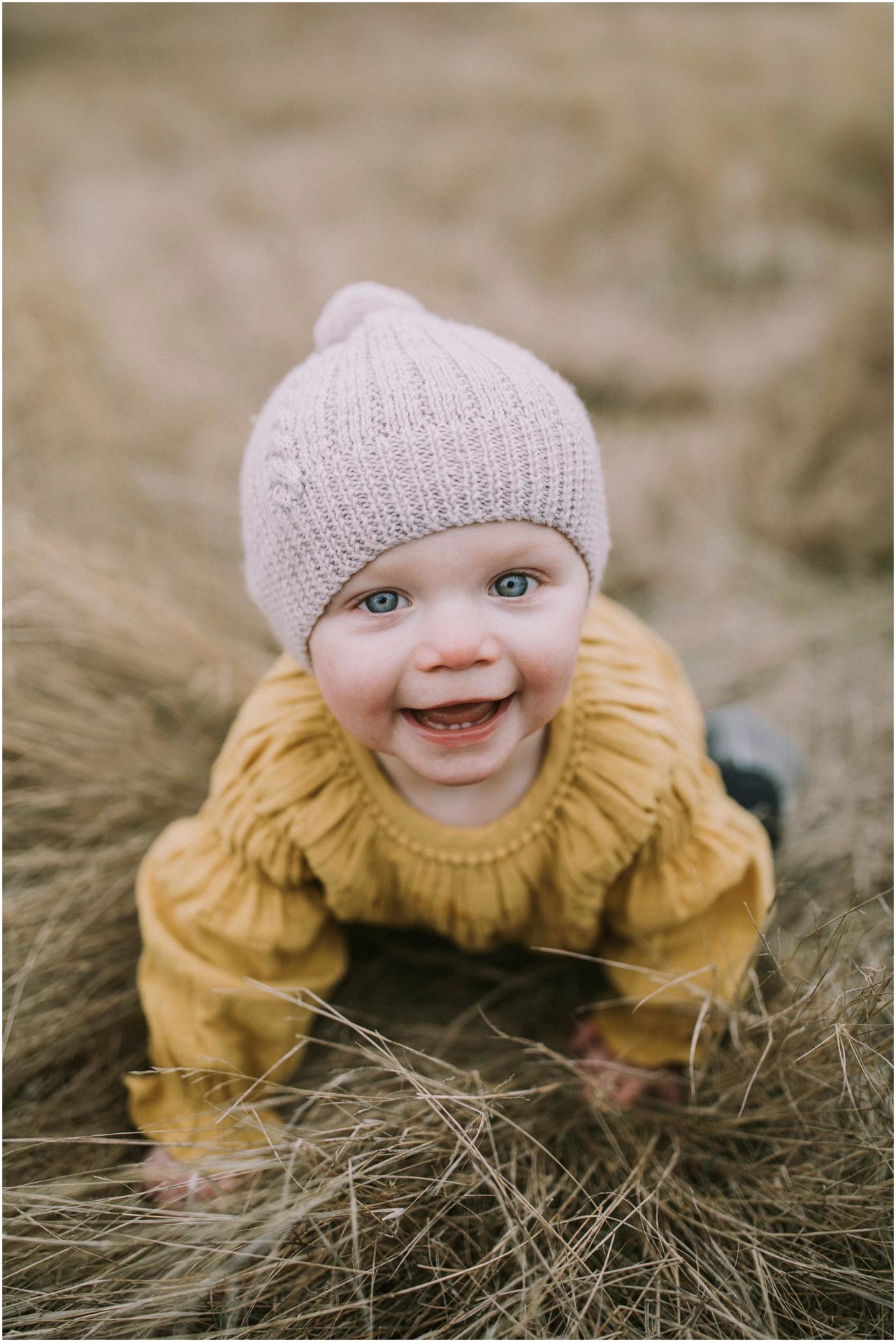 Charlotte Kiri Photography - Family Photography of a young child looking up happily as they crawl in the hay in Wanaka, New Zealand.