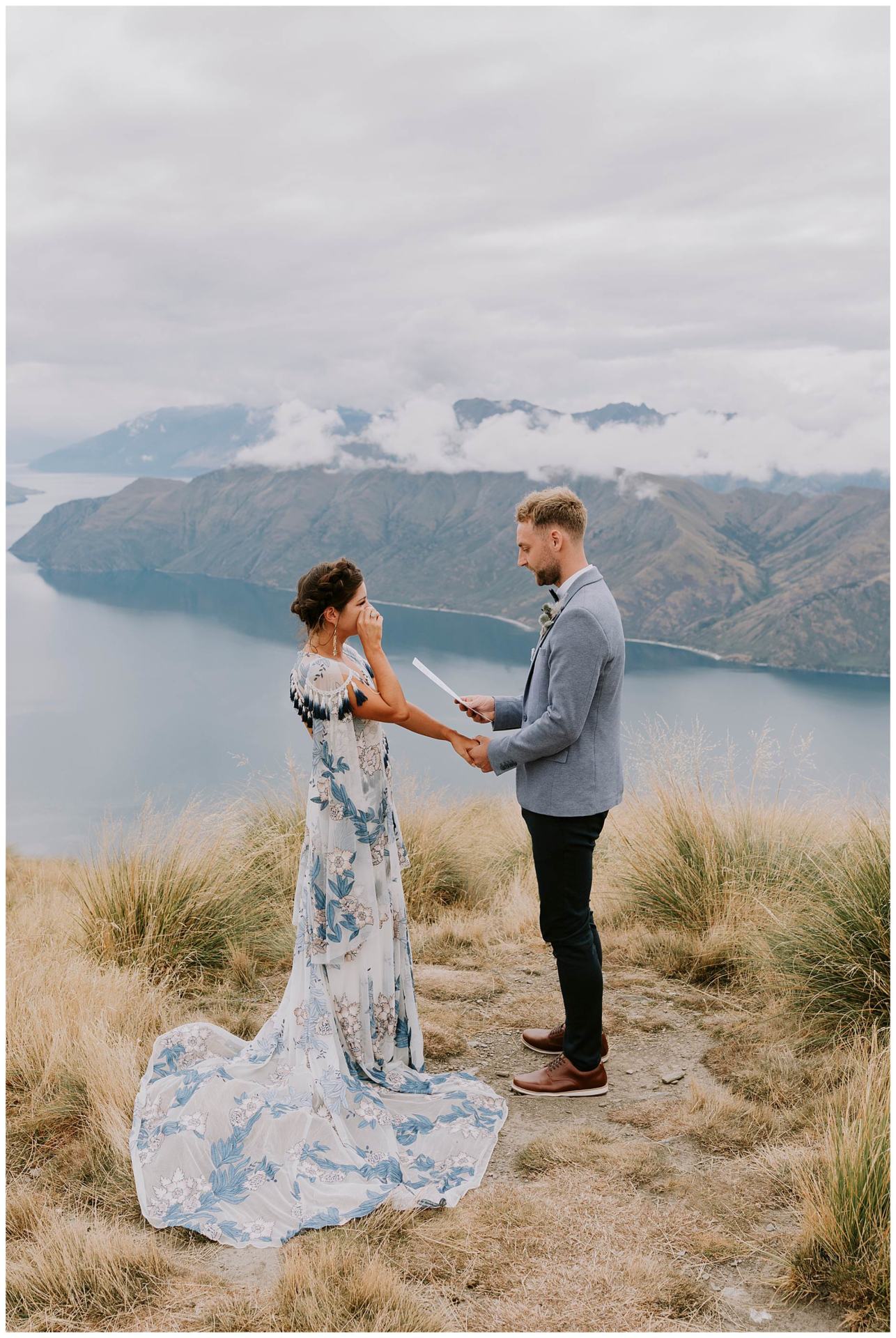 Charlotte Kiri Photography - Elopement Photography with the groom reading vows to his emotional bride on top of Roy's Peak, which overlooks a beautiful lake and mountain view in Wanaka, New Zealand