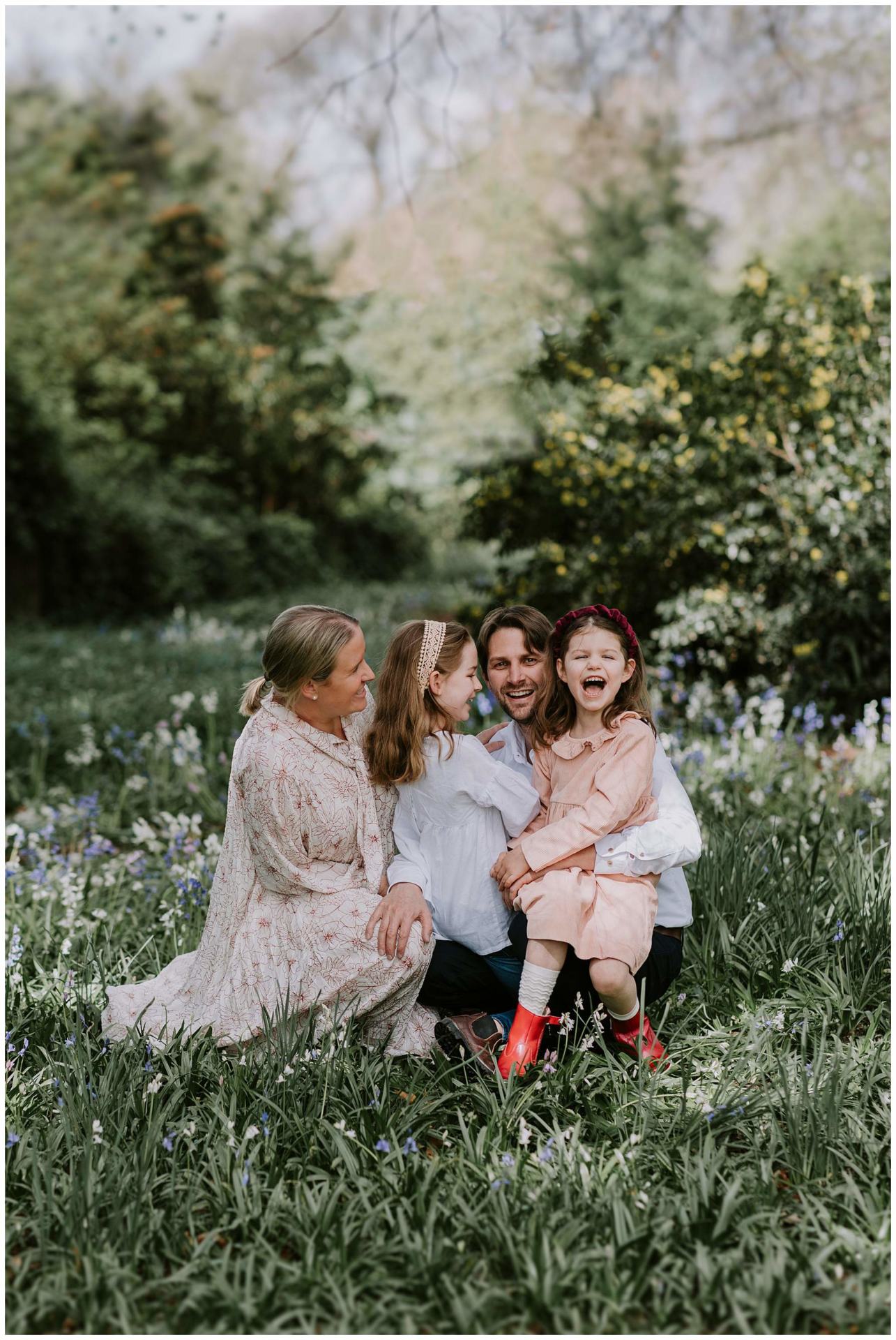 Charlotte Kiri Photography - Family Photography of a couple sitting in a field of flowers with their two young girls as they laugh together in Wanaka, New Zealand.