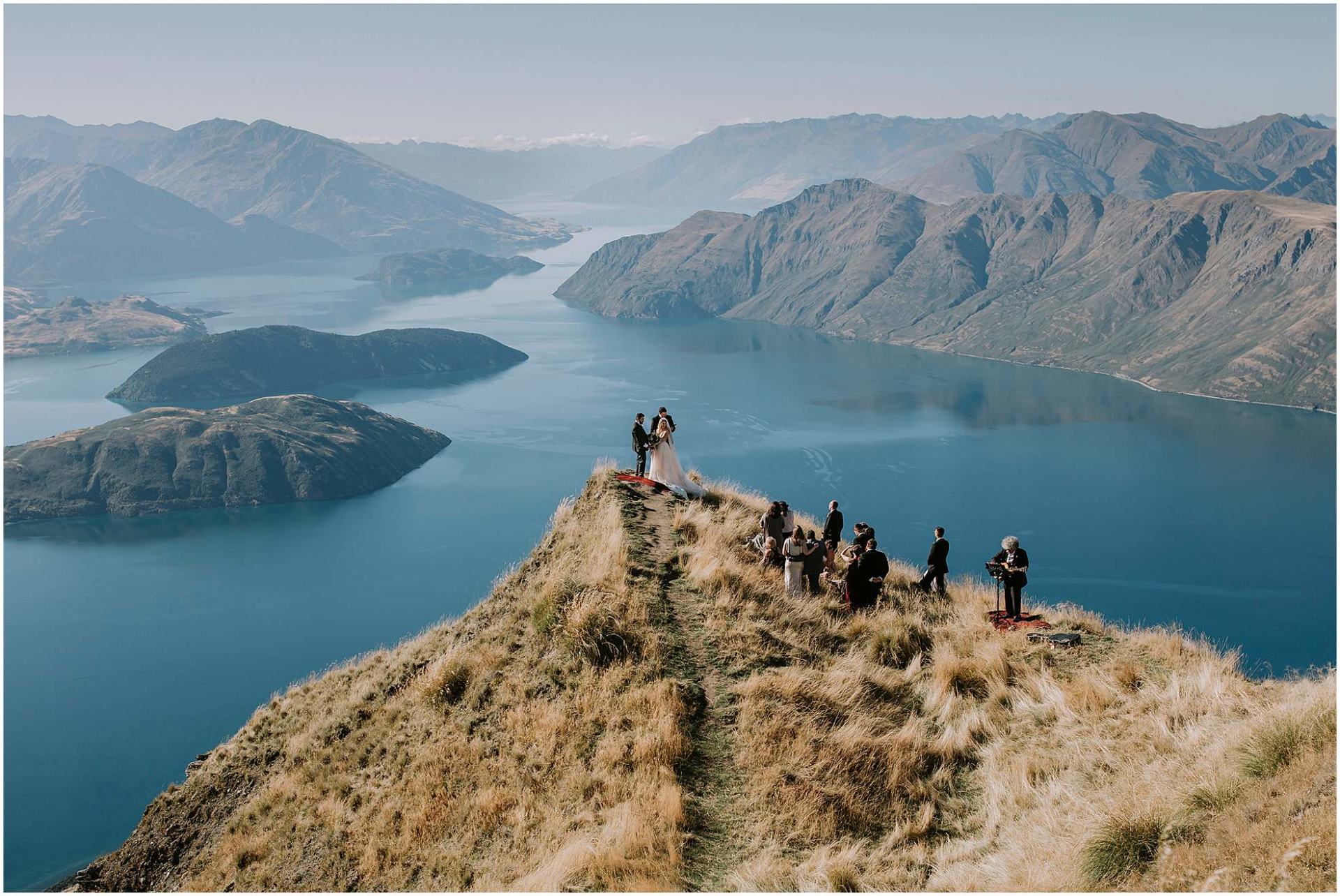 Charlotte Kiri Photography - elopement photography bride and groom exchanging vows in front of family and guests on top of Roy's Peak with glacial lakes behind, Wanaka, New Zealand